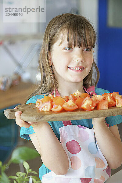 Smiling Young Girl Holding Chopping board with Tomatoes