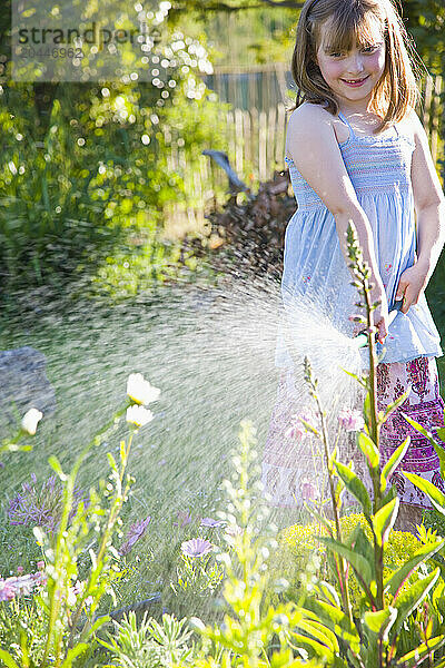 Young Girl Watering Flowers with Garden Hose