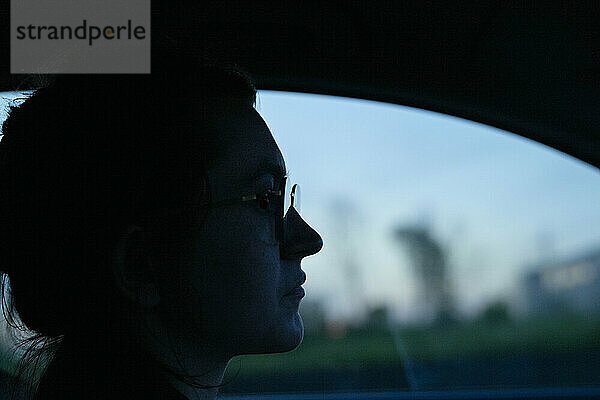 The image displays a profile view of a person sitting inside a vehicle during twilight with a blurred background.