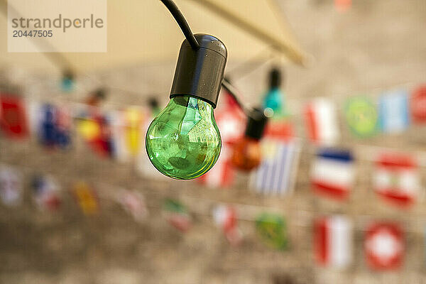 A green light bulb hangs in focus against a blurred background festooned with colorful bunting flags.