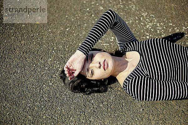 A person is lying on the ground wearing a black and white striped long-sleeve shirt  with their head resting on their arm  looking at the camera.