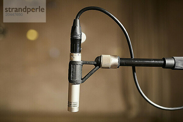 A close-up of a microphone connected to a cable with a blurred background  indicating a music recording or performing environment.