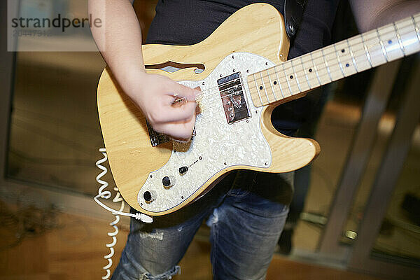 A close-up of a person strumming an electric guitar with a pick  focused on the guitar and strumming hand with a blurred background.