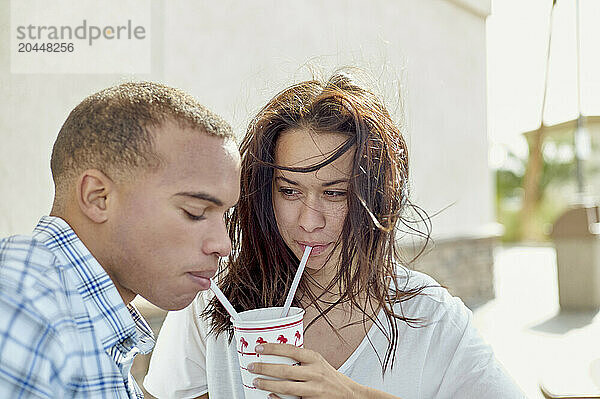 A man and a woman are sitting close together  sharing a beverage with two straws  with a clear bonding moment portrayed.