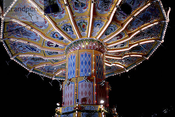 A vibrant and illuminated swing ride at night  with its chairs in motion creating a blur  lights sparkling brightly  and ornate designs decorating its surface.