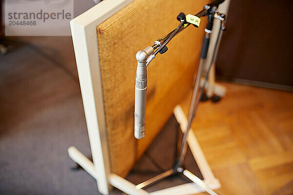 A close-up image of a silver microphone set up in front of a beige speaker cabinet on a wooden floor  with selective focus and blurred background.