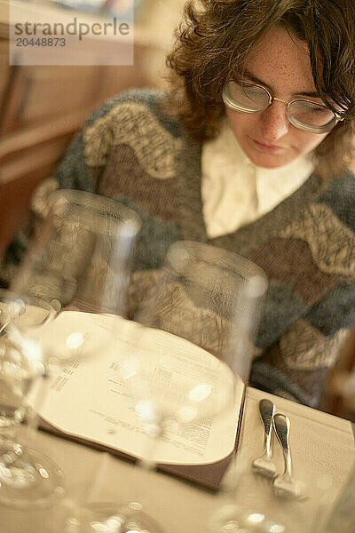 Woman focused on reading a menu at a warmly lit restaurant table