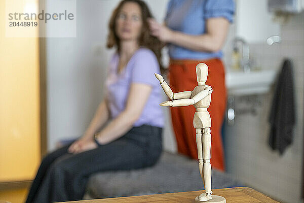 Mannequin figure in focus with hairstyling session in the background