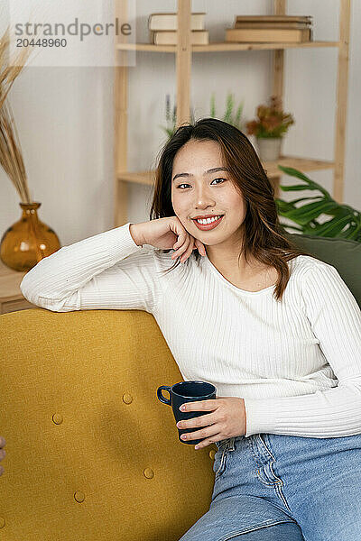 Smiling woman sitting with a cup on a yellow couch.