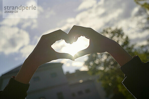 Hands forming a heart shape against a soft sky backdrop