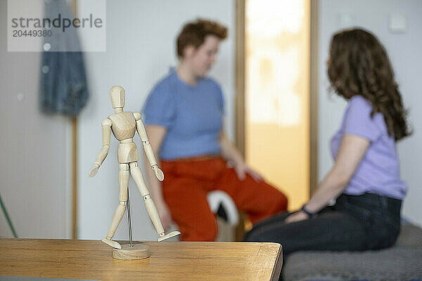 Wooden mannequin in focus with two blurred people in the background