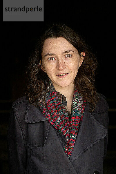 Smiling woman in a coat standing against a dark background.