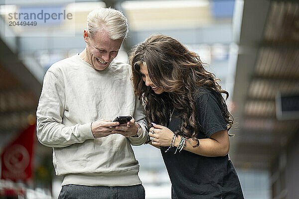 Two people laughing and looking at a phone together outdoors.