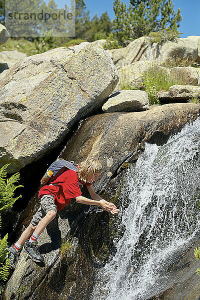 Young child in outdoor clothing climbing a rocky waterfall with a clear blue sky in the background.