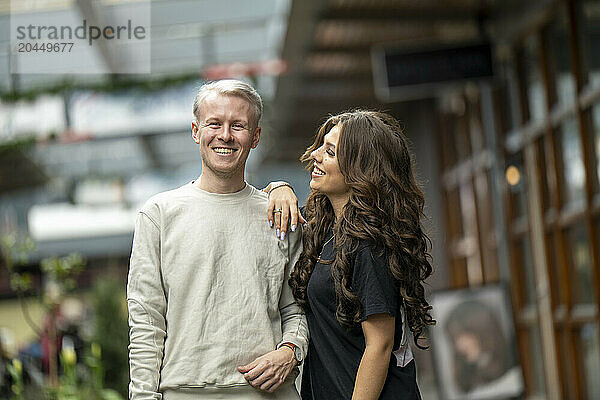 Smiling couple embracing in a cozy outdoor shopping area.