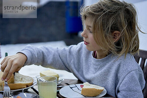 A young child is enjoying a meal at a table  reaching out for some bread.