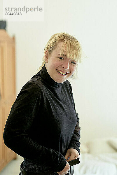 Smiling young woman in a black turtleneck standing indoors with a neutral background.