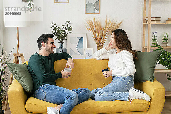 Two people laughing and chatting on a yellow sofa.