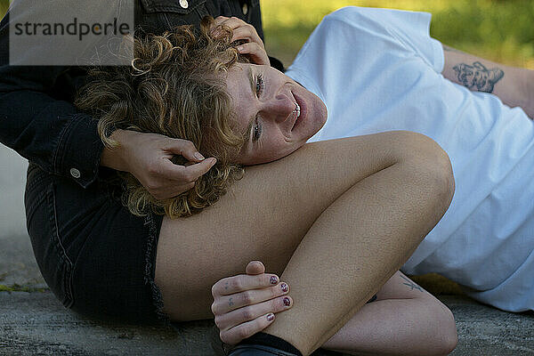 Smiling woman lying on someone's lap outdoors  enjoying a casual  affectionate moment.