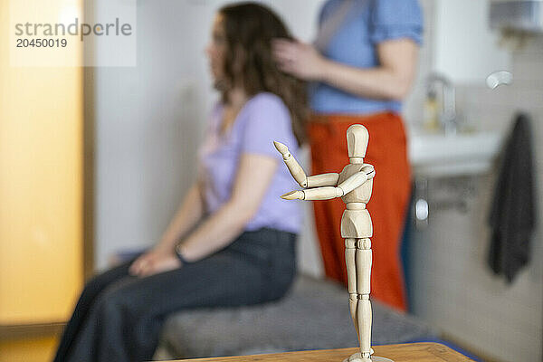 Wooden mannequin in focus with blurry hairstyling session in background