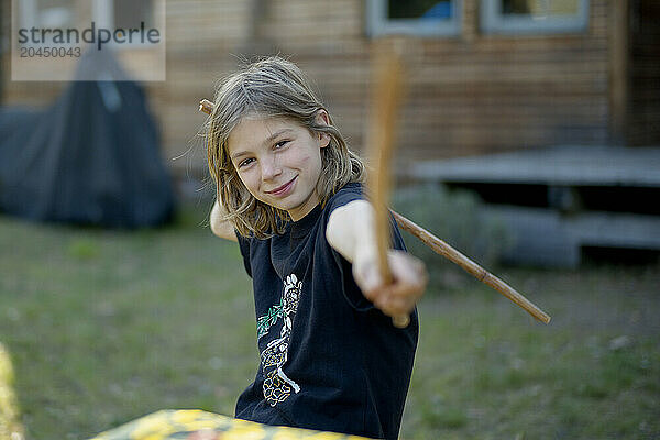 Smiling child reaching out with a wooden stick in a backyard setting.