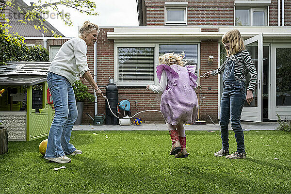 An adult is playing with two children in a backyard garden  spinning around a young girl who is laughing while another child watches.