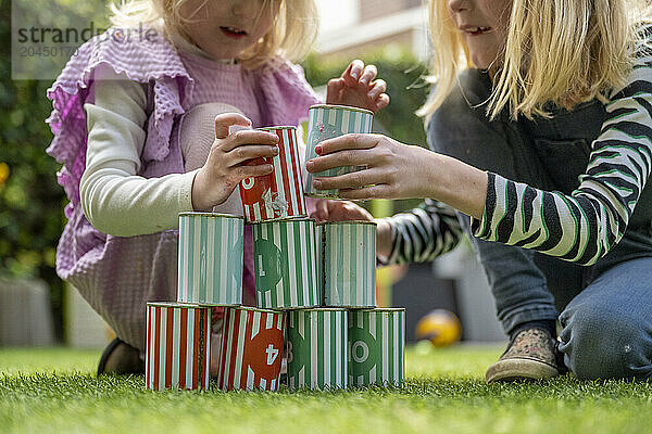 Two children are playing with colorful stacking cups on a grass lawn  focusing intently on building a structure.