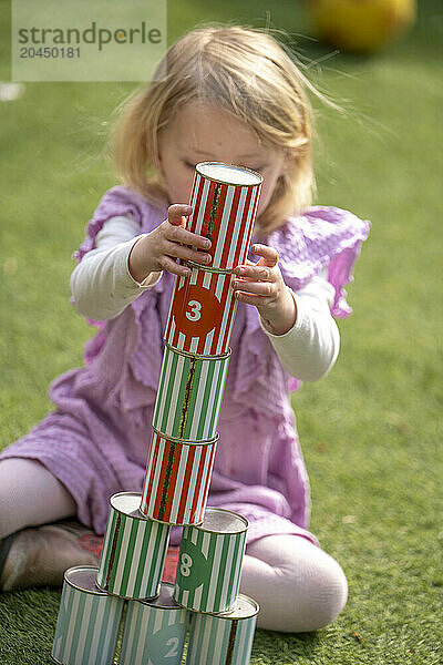 A young girl is playing outside  stacking colorful numbered cups on a grassy surface.