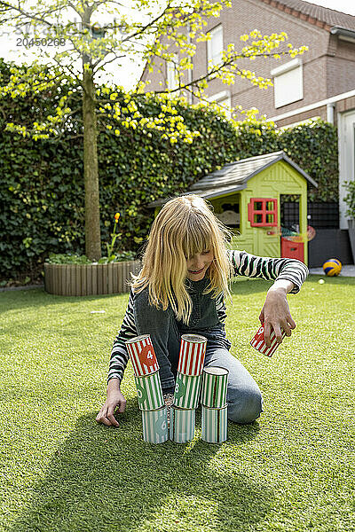 A child is playing with colorful blocks outdoors  intently focused on stacking them on a grassy lawn with play equipment in the background.