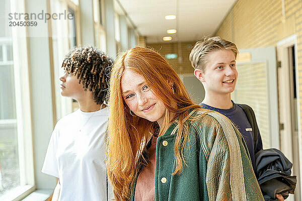 Three students standing in a school corridor  smiling and posing for the photo with a brightly lit background.