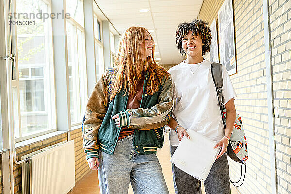 Two cheerful students walking down a school corridor  engaging in a friendly conversation with books in hand.