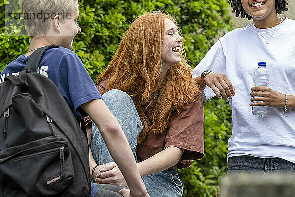 Three teenagers laugh and enjoy each other's company outdoors on a sunny day  with one holding a water bottle.