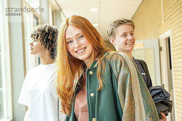 Three teenagers stand in a school corridor  smiling and looking relaxed  with backpacks suggestive of a break between classes.