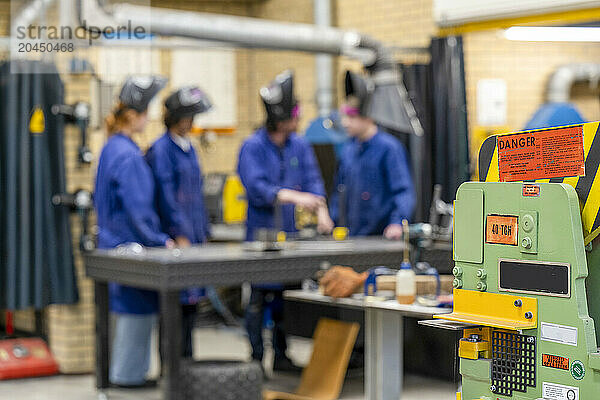 A group of individuals in safety gear are focused on work at a manufacturing workshop  with a prominent green machine in the foreground.