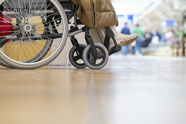 Close-up of a wheelchair with a person's legs  indoors with a blurred background of a public space.