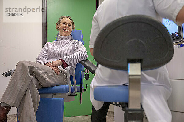 Smiling woman seated in a medical office  interacting with a healthcare professional.