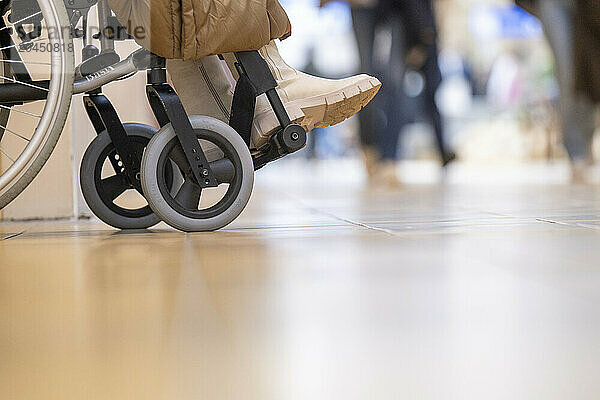 Close-up of a person in a wheelchair at a public facility with passersby in the background.