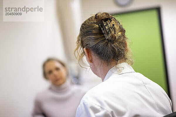 A woman with her hair up in a clip is seen from behind  in focus  with another woman out of focus in the background.