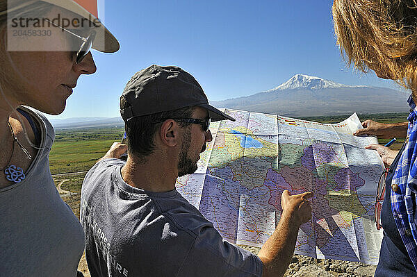 Guide explaining geography with a map to a tourist group  in front of the Turkish border and Mount Ararat at Khor Virap Monastery  Ararat plain  Artashat  Armenia  Eurasia