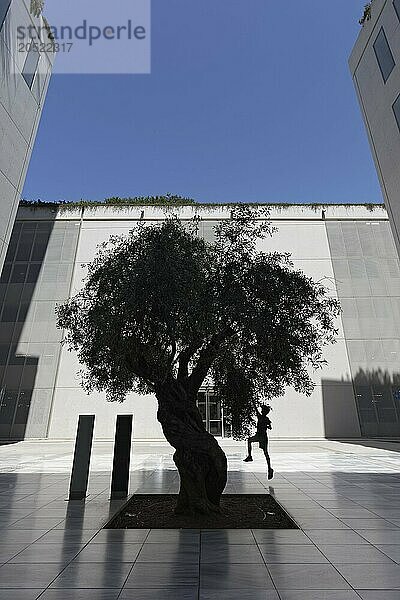 Junge springt hoch und greift nach den Blättern eines Olivenbaums  Silhouette zwischen moderner Betonarchitektur  Kulturzentrum der Stavros Niarchos Stiftung  Architekt Renzo Piano  Kallithea  Metropolenregion Athen  Griechenland  Europa