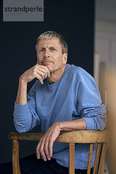 Retired senior man sitting on wooden chair at home