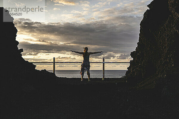 Young woman with arms outstretched standing under cloudy sky at Canary island