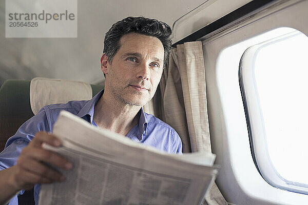 Confident mature businessman with newspaper sitting in airplane