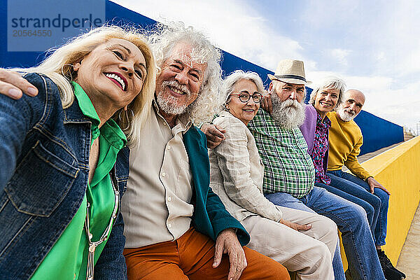 Cheerful senior friends sitting together on wall