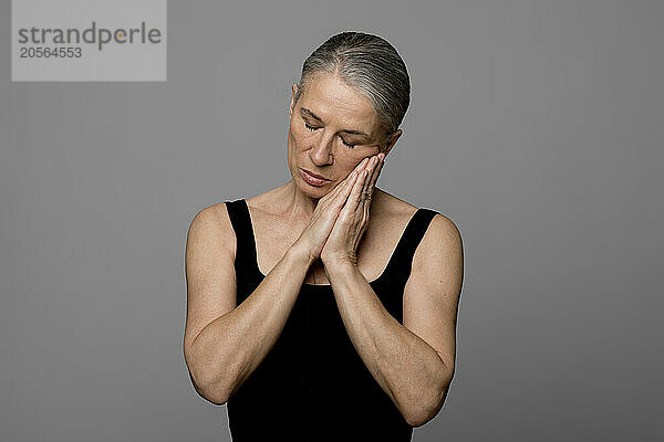 Senior woman with hands clasped standing against gray background