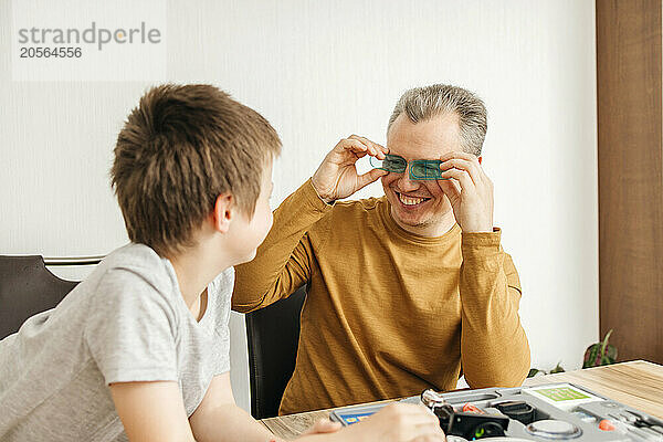 Happy man holding lens on eyes and playing with son at home