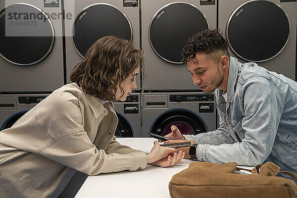 Young couple using smart phones leaning on table at laundromat