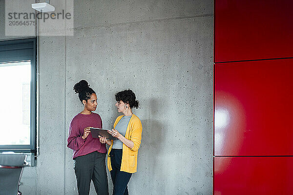 Entrepreneurs discussing over tablet PC in front of wall at office