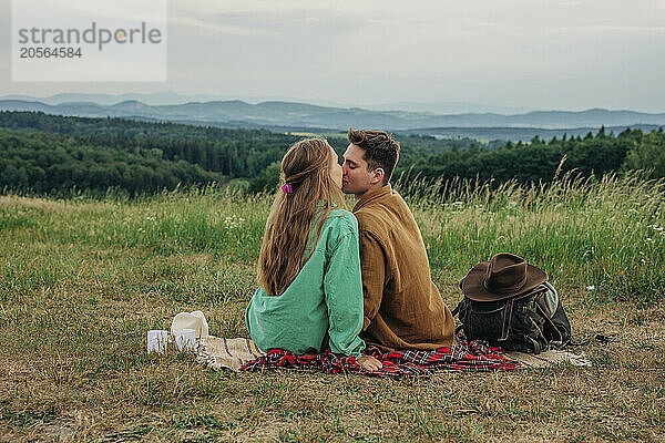 Affectionate young couple sitting and kissing on mountain of Poland