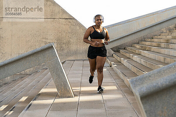 Sporty muscular woman jogging on footpath by steps